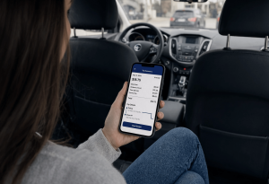 A passenger in the back seat reviews a rideshare trip summary on her phone, showing a $18.75 fare breakdown with pickup and drop-off details.