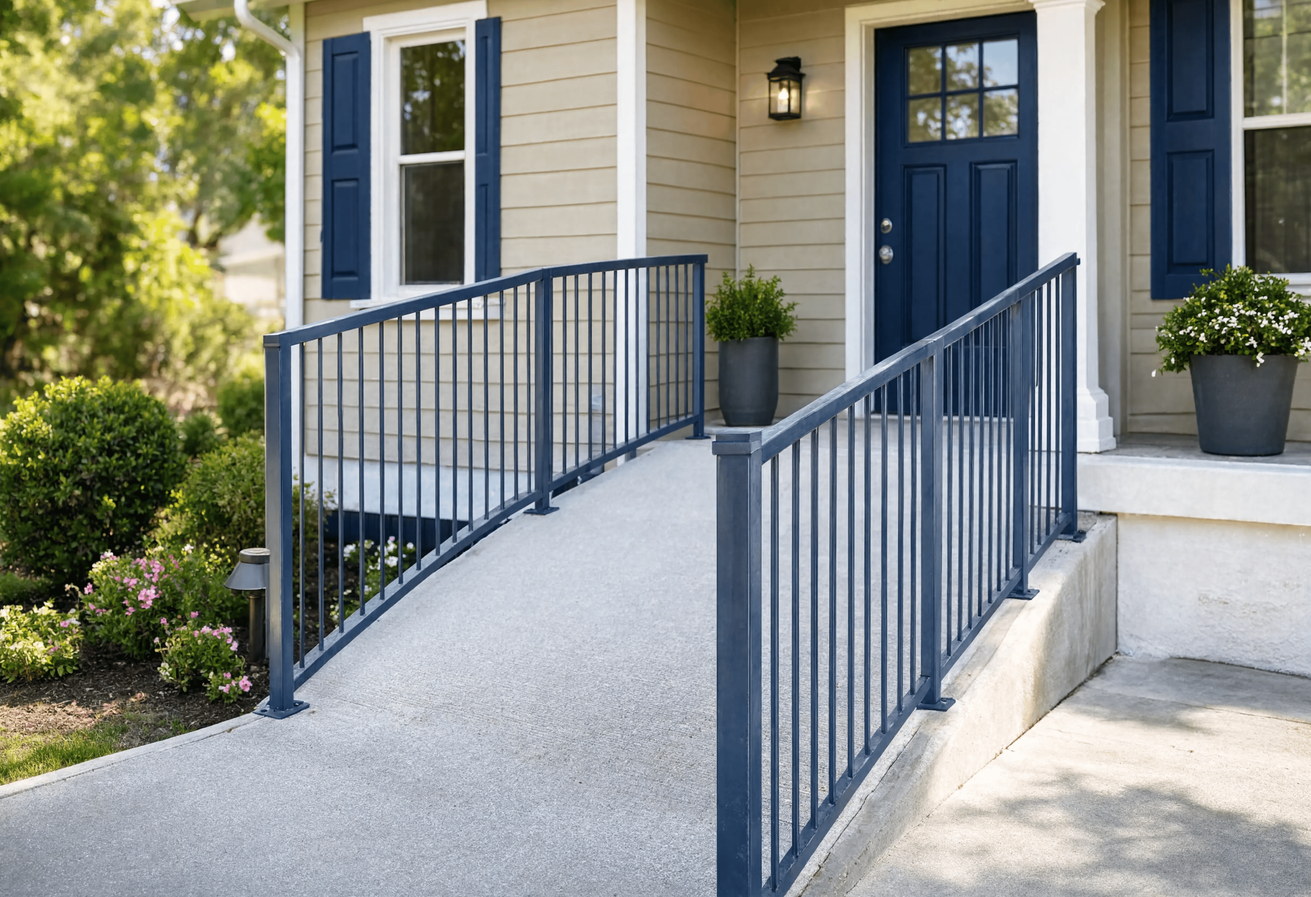 A wheelchair-accessible ramp with blue metal railings leading to the front door of a suburban home, flanked by manicured shrubs and potted plants.